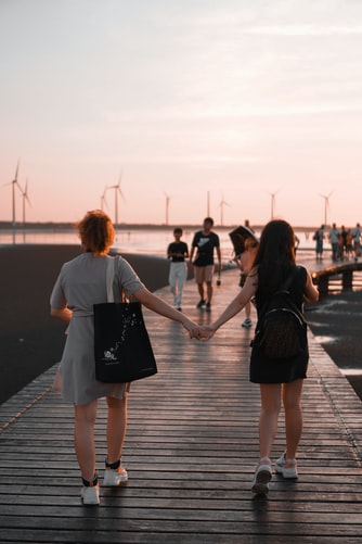 Two women holding hands while walking towards the beach