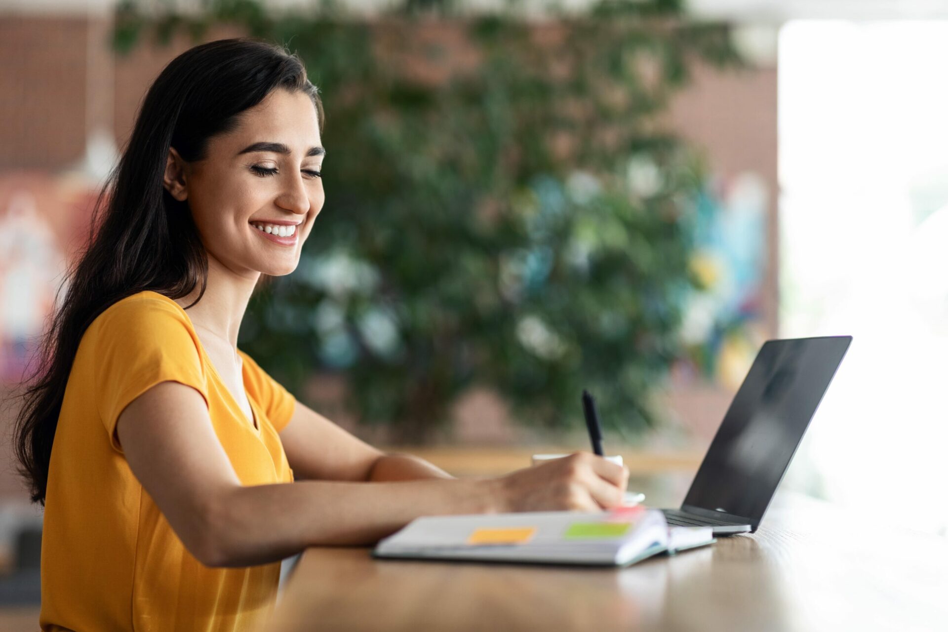 Female writing on notebook and in front laptop