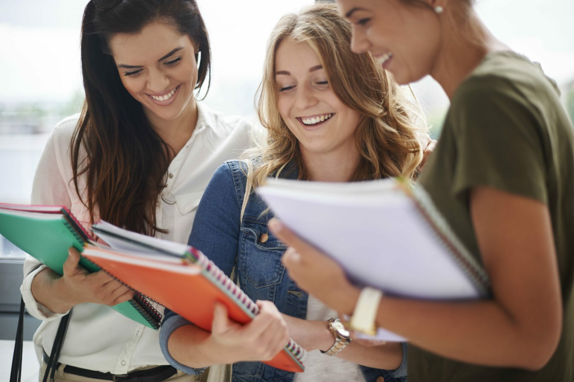 3 female students carrying notebooks and smiling