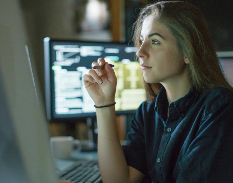 A woman staring intently to her pc while holding a pen.