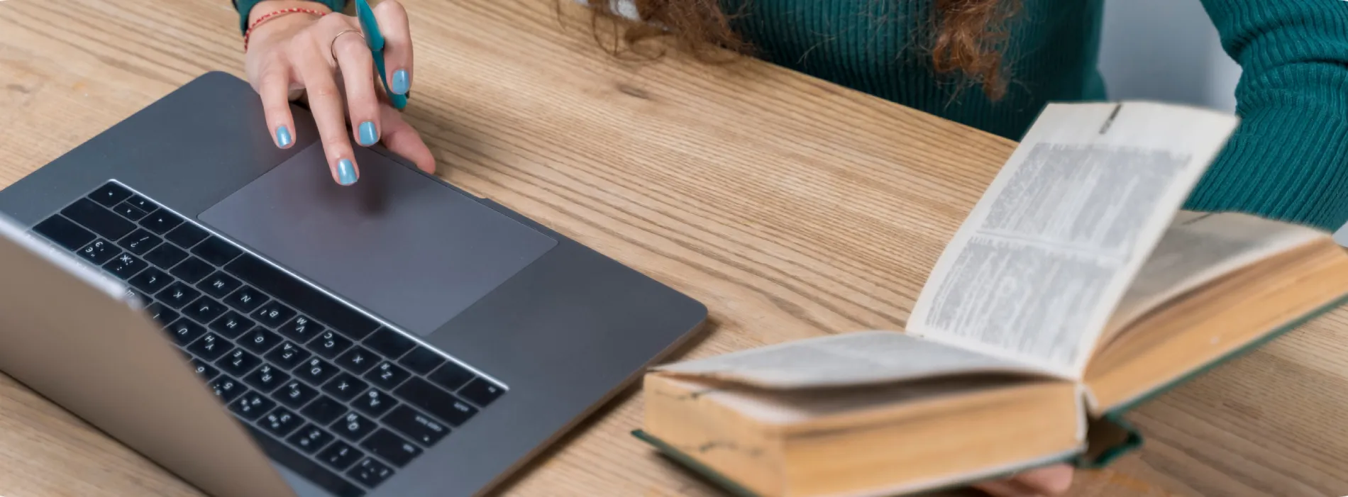 A person holding a book while doing something in her laptop