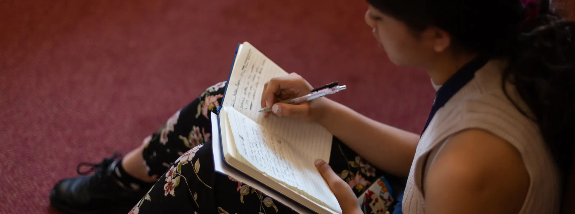 A woman sitting on the floor writing on her notebook.