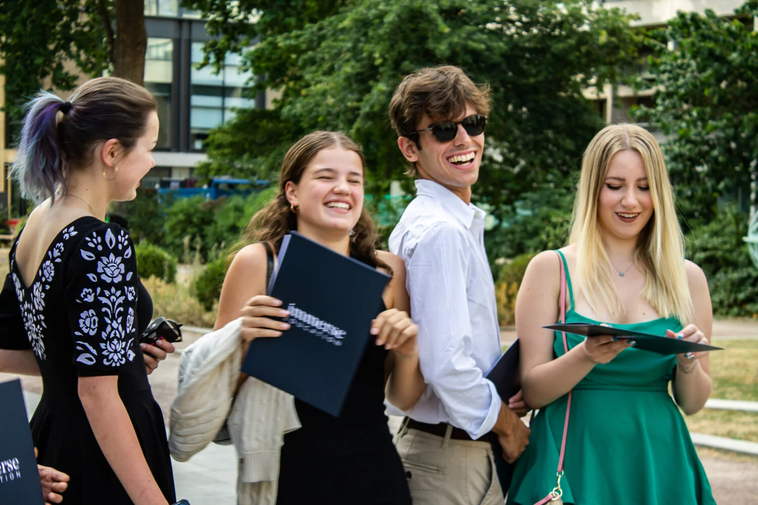 Four students holding a diploma laughing.