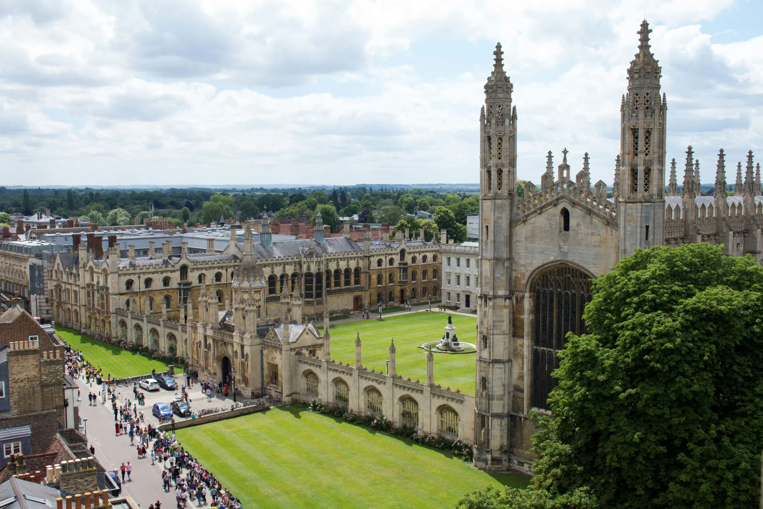 a large building with towers and a lawn with people walking around