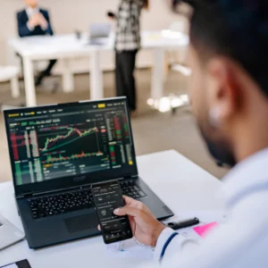 a person holding a phone in front of a laptop that shows stock finance