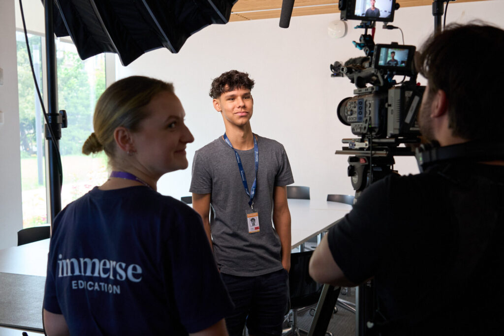 A year 12 student stands behind cameras and camera operators as he is filmed for work experience.