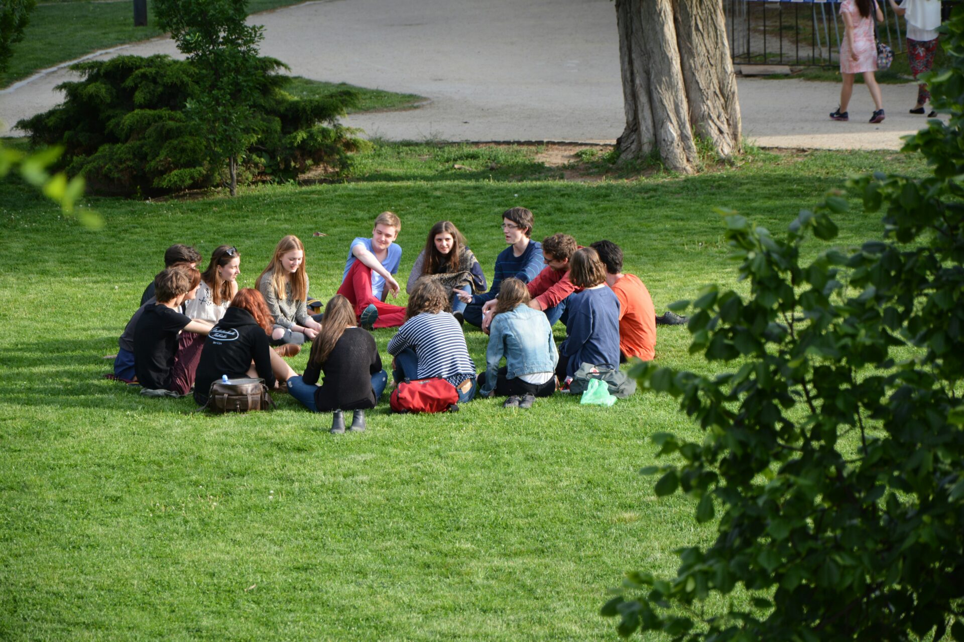 A group of high school students sit in a circle on the grass in a park, discussing things for high schoolers to do over the summer.