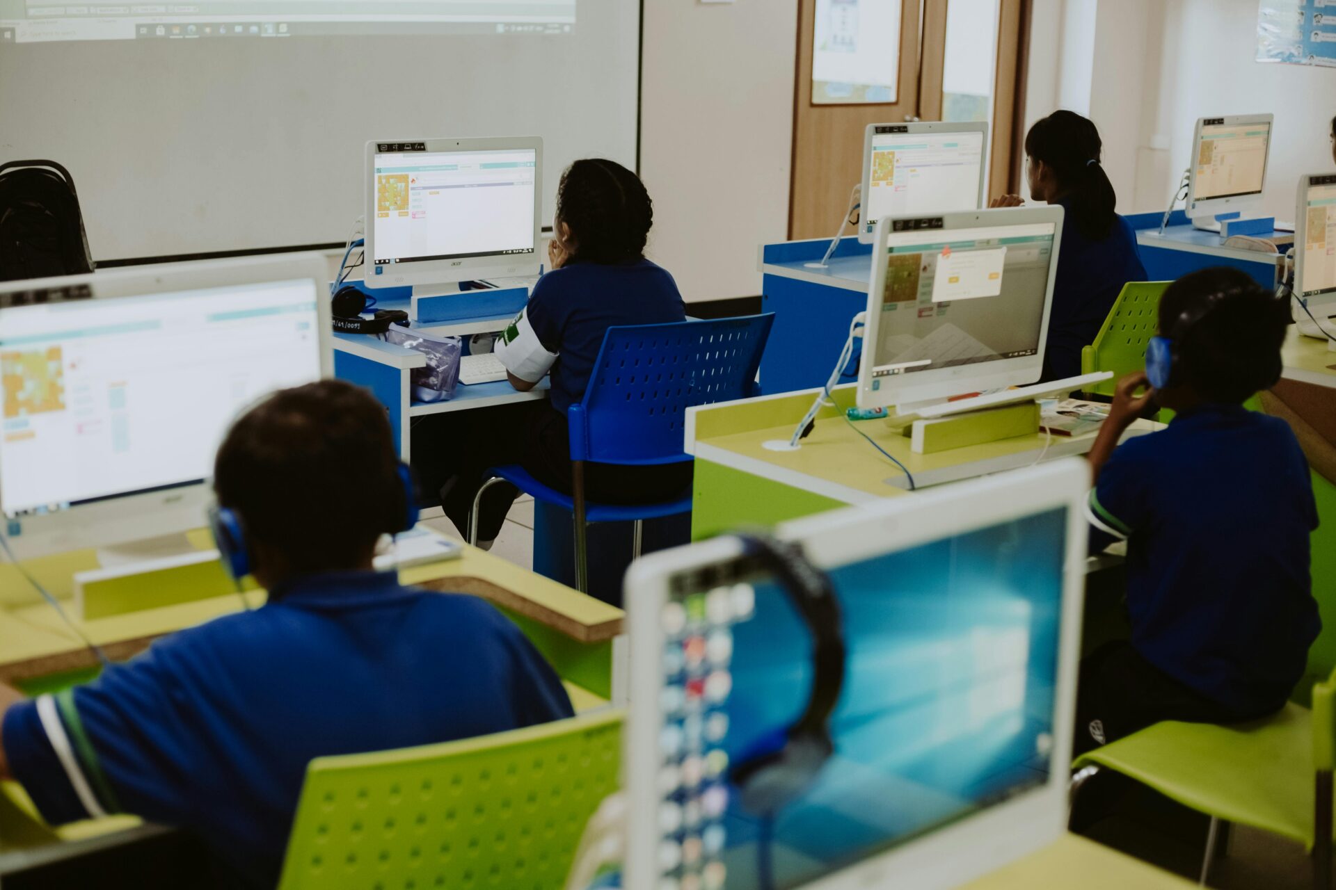High school students in a computer lab, learning how to do research as a high school student, with some wearing headphones and focused on their screens.