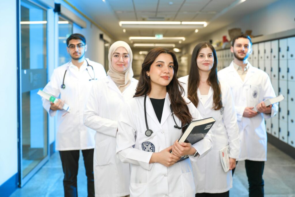 A diverse group of medical students in white coats and stethoscopes standing in a hallway, representing summer opportunities for medical students.