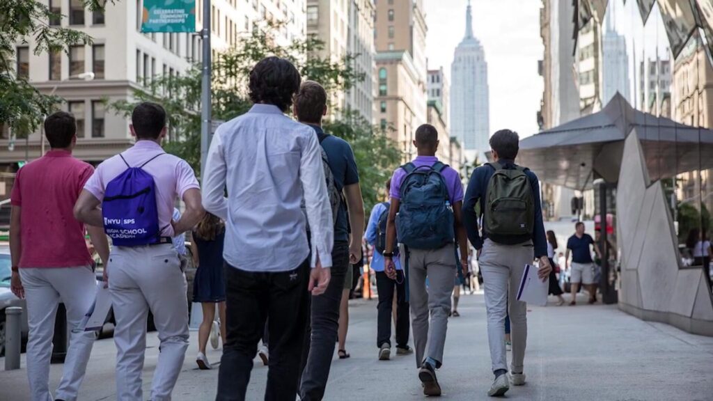 A group of six students walking on an NYC street with their backs to the camera