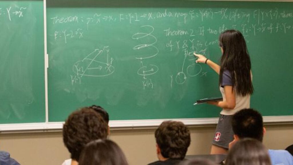 An instructor explaining math concepts on a chalkboard as students listen