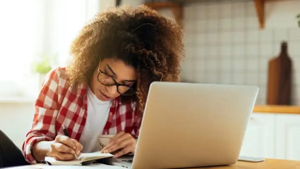 A student taking an online on their laptop and taking notes