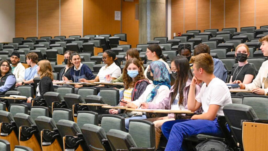 A group of students sitting in classroom chairs and conversing among each other