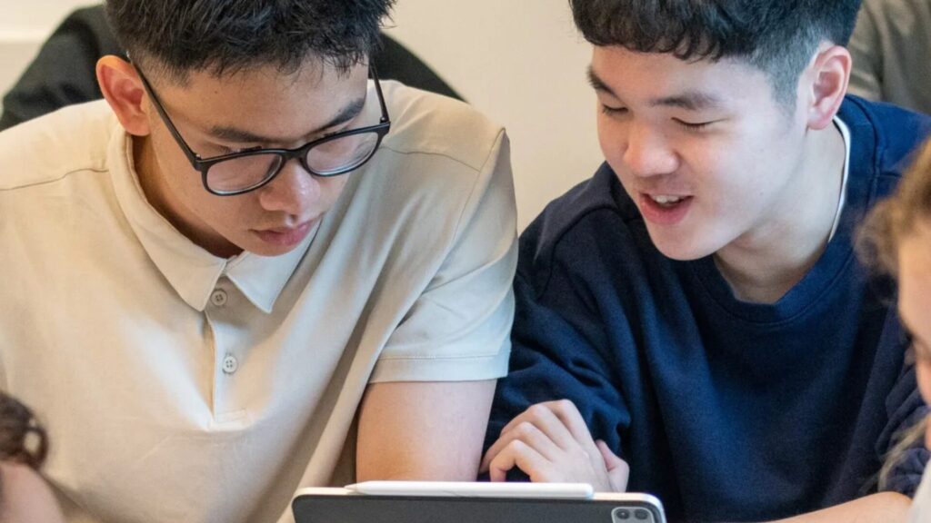 Two students sitting next to each other and looking at something on an ipad together