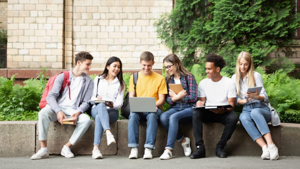A group of students sitting together on a bench, with one of them holding a laptop