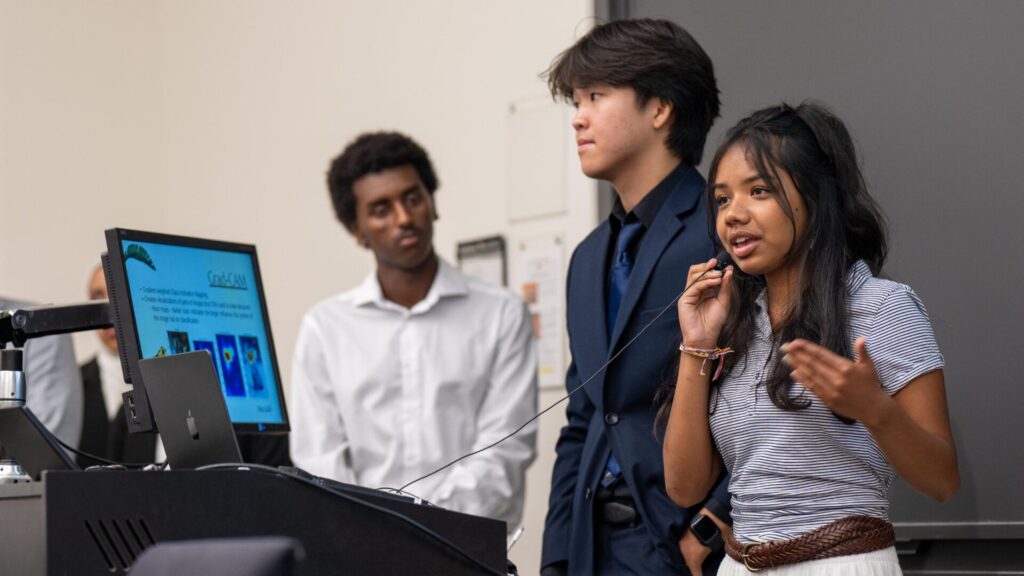 A group of three students doing a presentation using a mic and a laptop