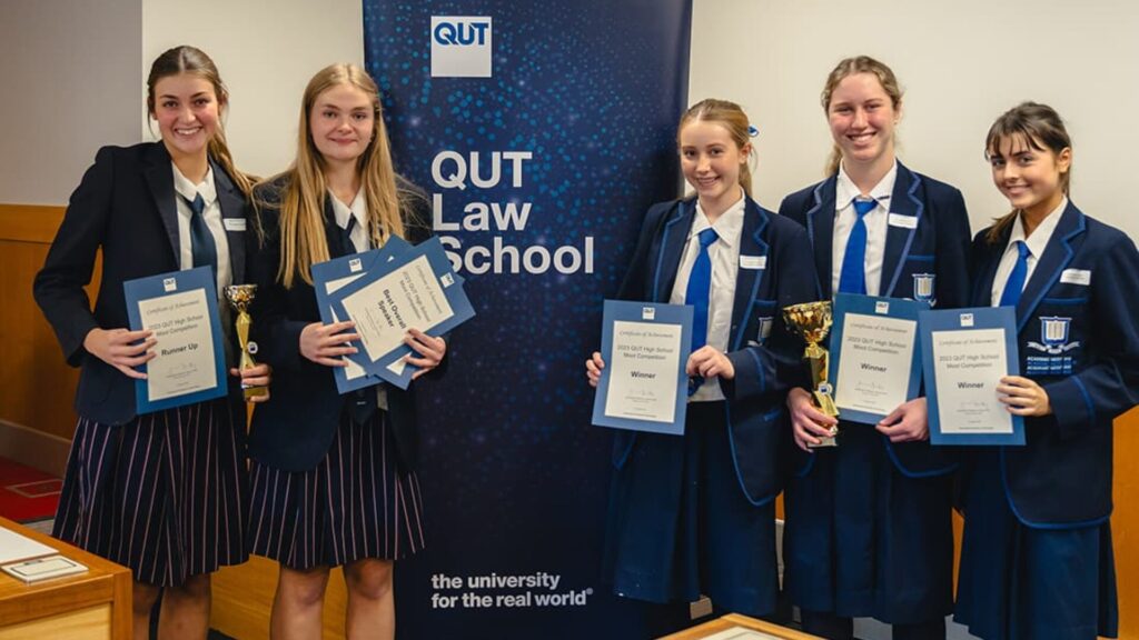 Five students standing together, wearing blue blazers, and holding certificates