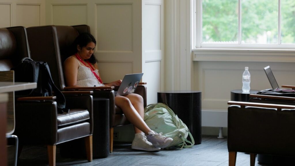 A student sitting on a sofa with a laptop on their lap, attending an online class