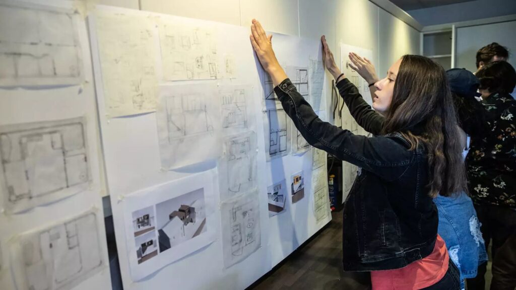 A person hanging up a diagram of architectural designs on a board
