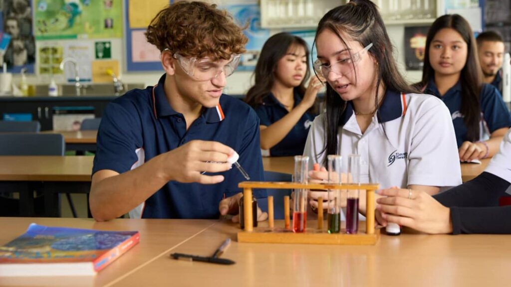 Two students sitting next to each other in a class, with beakers in front of them