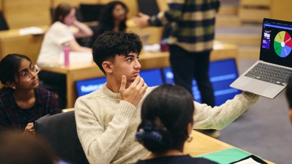 A student presenting something on their laptop to the students sitting around them