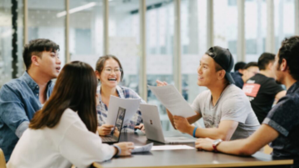 A group of students sitting around a table, chatting and laughing
