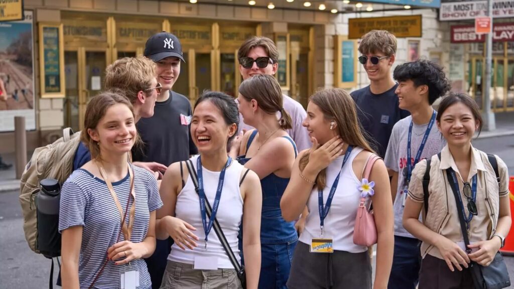 A collection of high-school students, gathered in a group, laughing and talking amongst themselves.