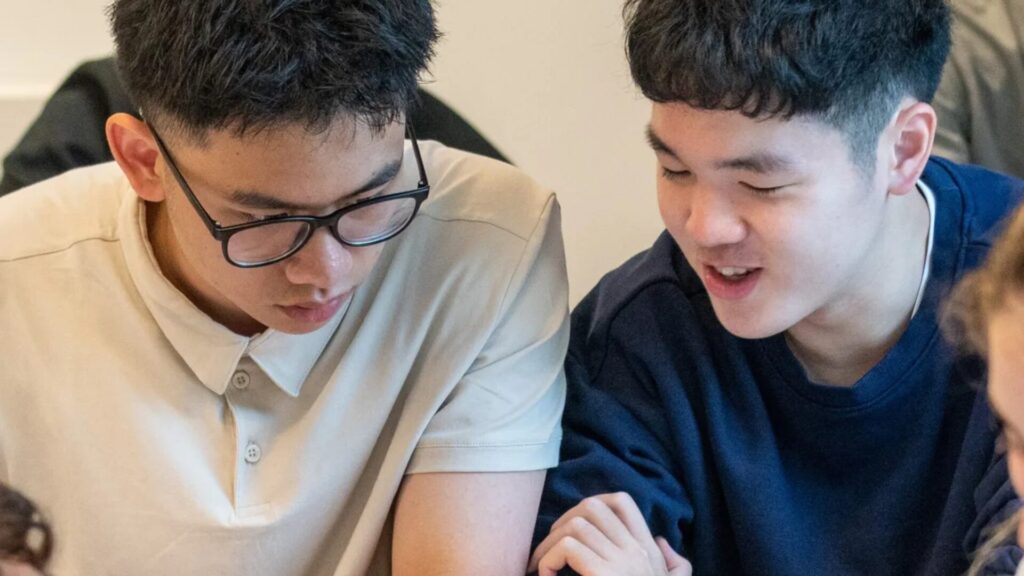 Two students sitting next to each other and looking at something on an ipad together