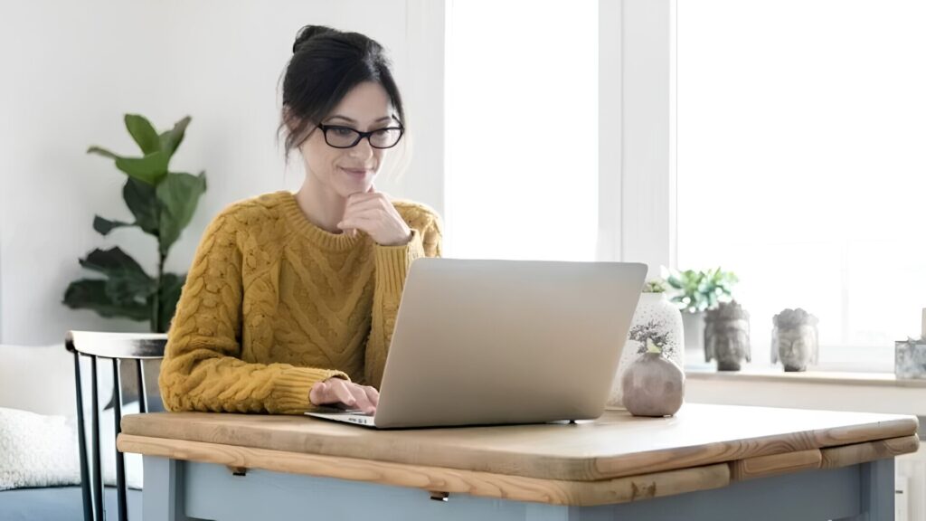 A student sitting next to a window with their laptop open in front of them