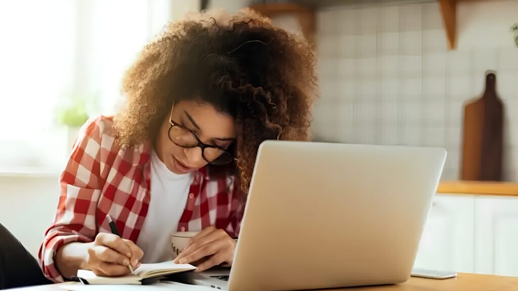 A student taking an online on their laptop and taking notes